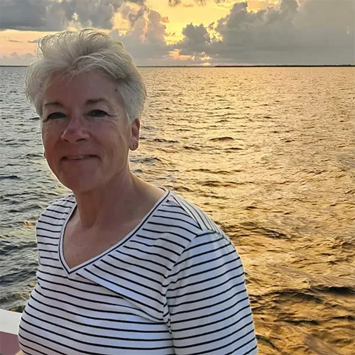 Deb Hamlin on boat with ocean sunset behind her